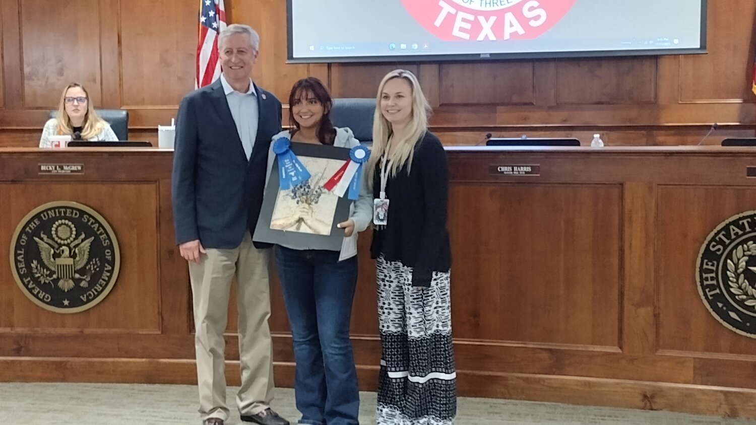 Katy Mayor Dusty Thiele (left) and Ashley Lipsman, City of Katy tourism and marketing event coordinator (right), recognize Mariam Elsherbiny (center) as the winner of the 2023 Katy Rice Harvest Festival art contest “Best of Show” for her art piece “Wildflowers.”